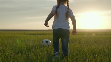 Little child plays soccer with soccer ball on the green field of the stadium at sunset, professional football team training, kid dynamic active training, fan life, learn how to score goal, kick ball.