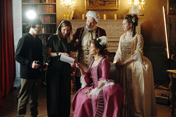Multiethnic group including young adult woman in Baroque dress sitting and holding script while...