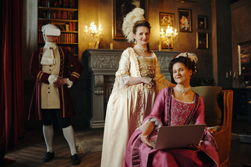 Caucasian middle aged woman in ornate Renaissance dress sitting with laptop, Caucasian middle aged...