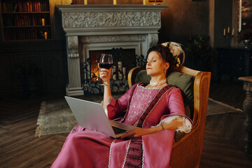 Caucasian middle aged woman wearing Baroque style dress sitting in ornate chair holding wine glass...