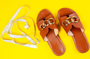 Women slippers top view with measuring tape on yellow background summer beach diet concept