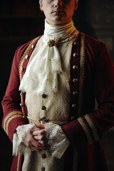 Caucasian young adult man standing with hands clasped wearing ornate Baroque style clothing...