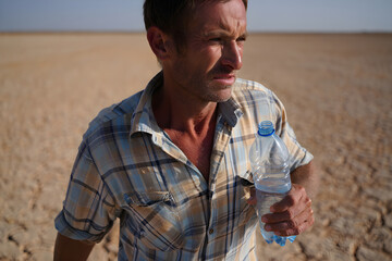 Weathered farmer gripping final water bottle amid cracked, arid farmland, symbolizing climate crisis and agricultural struggle