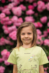 a girl with blonde hair is standing in front of a rose bush