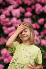 a little girl in a yellow T-shirt is laughing and holding her forehead, as if she had forgotten something, and then remembered