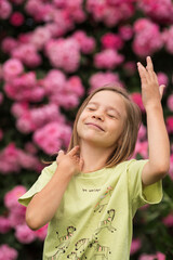 a girl is standing in front of a beautiful pink rose bush, waving her arms and having fun