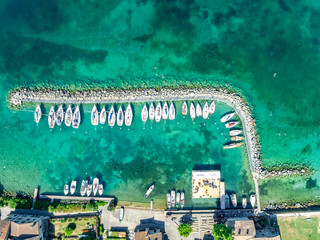 Aerial top down view of white sail boats docked in a crescent shape in a turquoise water harbor at...