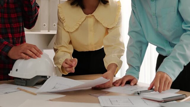 Architect and safety engineer discussion about building blueprint displaying on laptop on table with architectural document and wooden block scatter around at modern office. Closeup. Delineation.