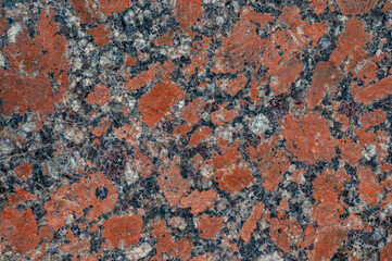 Close up texture of red granite stone with black and white flecks. The image shows a detailed view of the stone's surface, highlighting its color variations and mineral composition