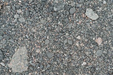 Close up view of dark gray gravel texture with small stones and fine particles. The image shows a variety of stone sizes and colors, creating a rough and uneven surface