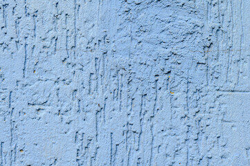 Detailed close up shot of a textured light blue wall. The surface is rough and uneven, with visible grains and small particles. The color is a consistent pale blue, with subtle variations in tone