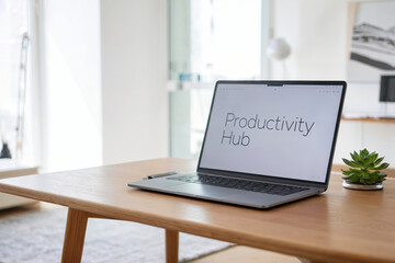 Fototapeta premium A minimalist workspace photograph featuring a silver laptop on a light wooden desk. The laptop screen displays the text 