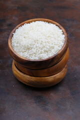 Raw white rice on black background. Long uncooked rice in wooden plate. Natural organic food. Traditional Asian cereal culture.