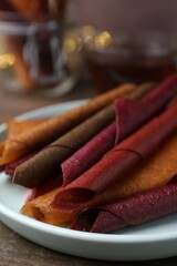 Tasty fruit leather rolls on wooden table, closeup