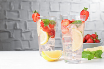 Tasty refreshing drink with strawberries, lemon and mint on white table, space for text