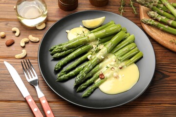 Tasty cooked asparagus served with lemon and sauce on wooden table, closeup