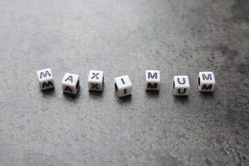 Word Maximum made of cubes on grey table, closeup
