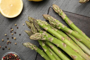 Fresh raw asparagus spears, lemon and spices on black table, flat lay