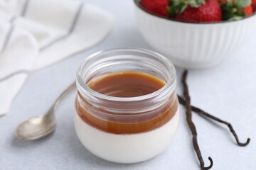 Tasty panna cotta with caramel, vanilla pods and strawberries on light table, closeup