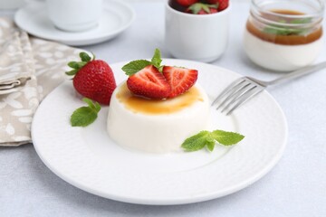 Tasty panna cotta with caramel, strawberries and mint on light table, closeup