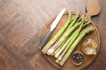 Fresh raw asparagus, spices, oil and knife on wooden table, top view. Space for text