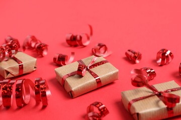 Shiny serpentine streamers and gift boxes on red background, closeup