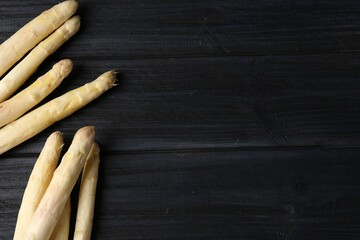 Raw white asparagus spears on black wooden table, flat lay. Space for text