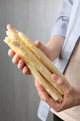 Woman with raw white asparagus spears on grey background, closeup