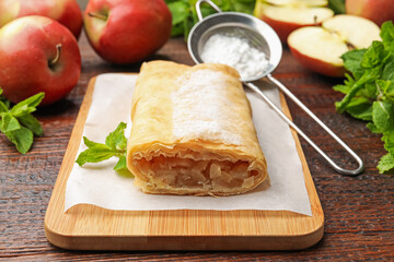 Tasty apple strudel with powdered sugar, mint and fruits on wooden table, closeup