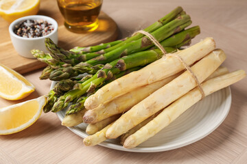 Different raw asparagus spears and spices on wooden table, closeup