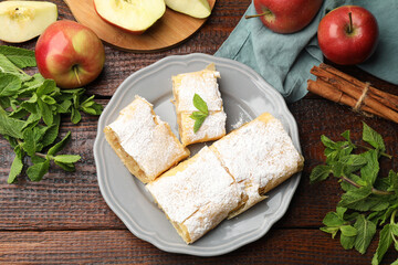 Pieces of tasty apple strudel with powdered sugar, mint and fruits on wooden table, flat lay