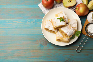 Pieces of tasty apple strudel with powdered sugar, mint and fruits on light blue wooden table, flat...