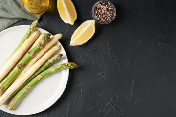 Green and white asparagus with spices on black table, flat lay. Space for text