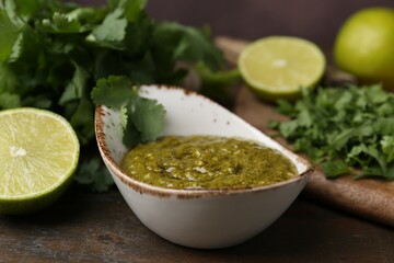 Tasty sauce with cilantro and limes on wooden table, closeup