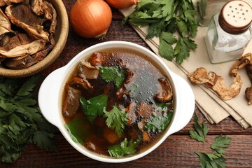 Tasty soup with mushrooms and parsley in bowl on wooden table, flat lay