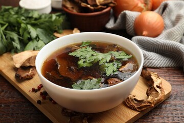 Tasty soup with mushrooms and parsley in bowl on wooden table, closeup
