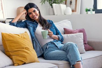 Obraz premium Pretty woman drinking a cup of coffee while sitting on couch in living room at home.