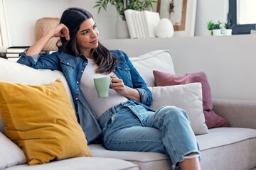 Obraz premium Pretty woman drinking a cup of coffee while sitting on couch in living room at home.