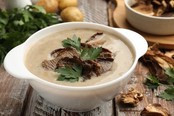 Tasty cream soup with mushrooms and parsley in bowl on color wooden table, closeup