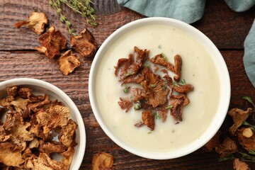 Tasty cream soup, thyme and dry chanterelle mushrooms on wooden table, flat lay