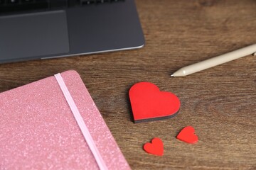 Decorative hearts, laptop, notebook and pen on wooden table, closeup. Online dating site
