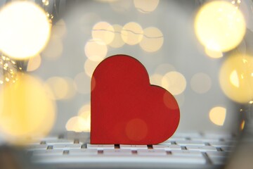 Online dating site. Wooden heart on computer keyboard against blurred lights, view through...
