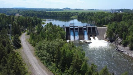 A view of a hydroelectric dam with cascading water and full-flow spillway gates, combining industrial design with a lush forest setting, showcases sustainable renewable energy production. Mitis-2 Dam. - Powered by Adobe