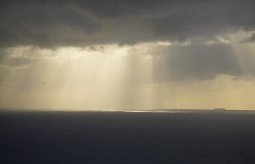 sun shines through distant clouds over the ocean , with ship in the rays of light