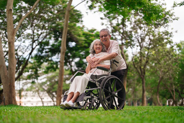 Asian older couple park enjoy outdoor time man supports woman wheelchair love care post retirement...