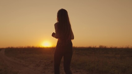 A girl in headphones runs along the road at sunset, a young woman makes a morning jog, a healthy lifestyle outdoors, a long-distance race, preparation for victory in a sports competition.
