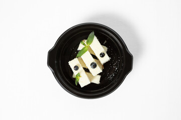 Coconut dessert bars topped with shredded coconut, served with blueberries and mint on a plate against a white background