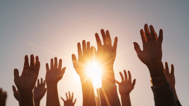 Many hands raised high against a bright sunset