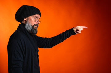 Expressive man with beard and glasses points with both hands on vibrant orange background....