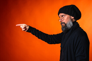 Expressive man with beard and glasses points with both hands on vibrant orange background....
